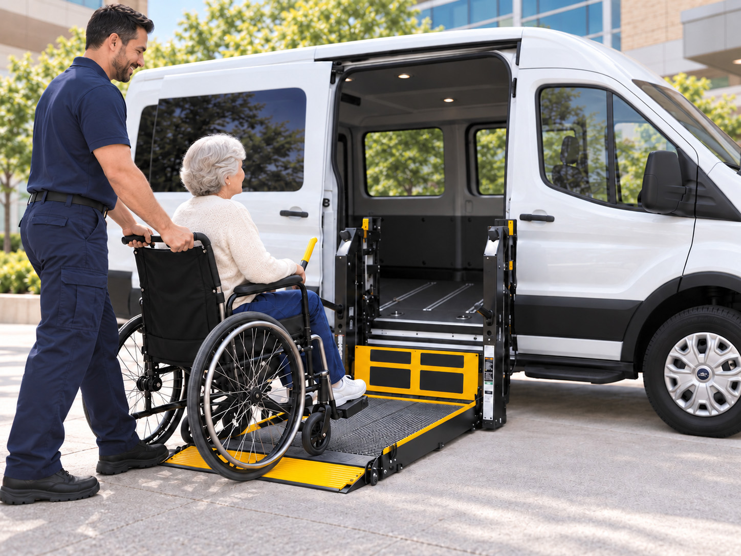 A driver helps an older woman in a wheelchair onto a van's lowered wheelchair lift
